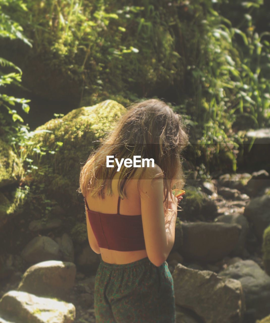 Rear view of woman standing by rock against plants