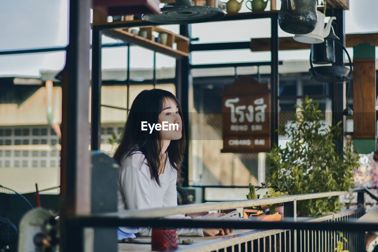 Woman looking away while sitting on window