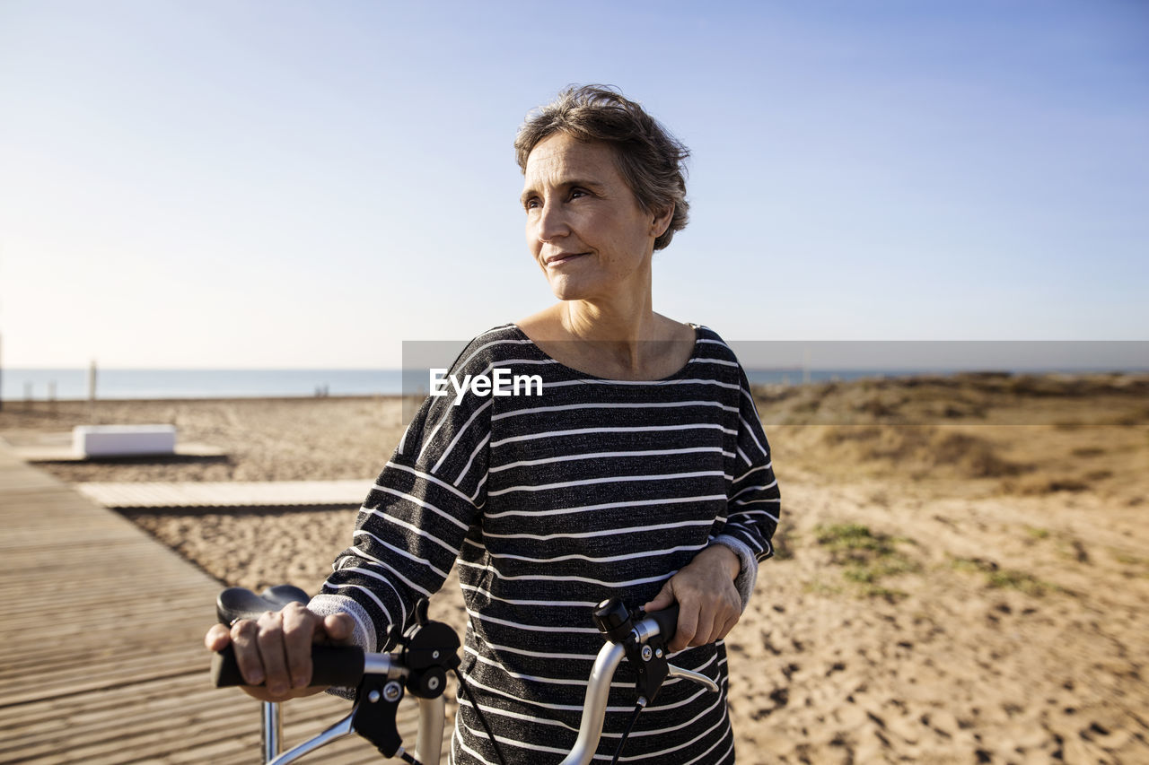 Woman with bicycle at beach against clear sky