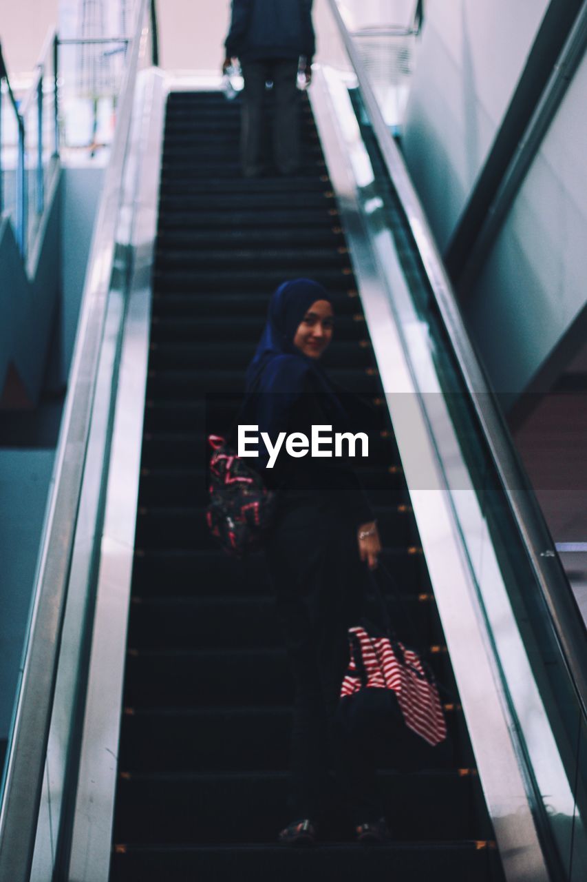 Low angle view of woman wearing hijab standing on escalator