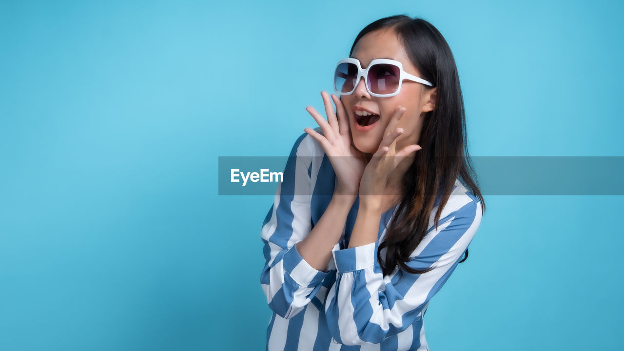 WOMAN WEARING SUNGLASSES AGAINST GRAY BACKGROUND