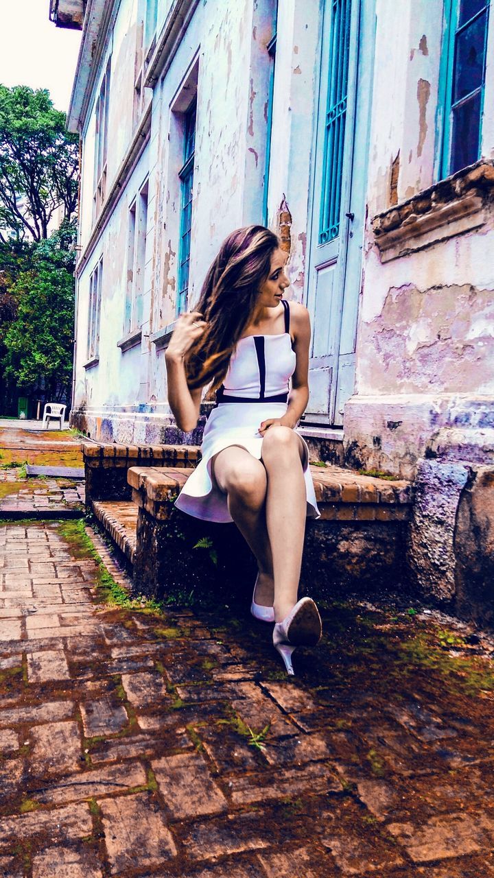 Beautiful woman sitting on retaining wall against abandoned building