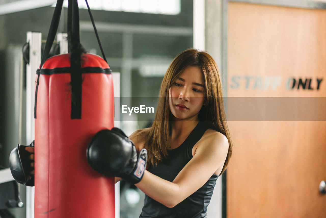 Confident young woman holding punching bag while standing in gym