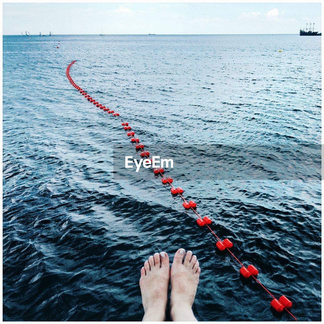 Low section of woman dangling feet over sea