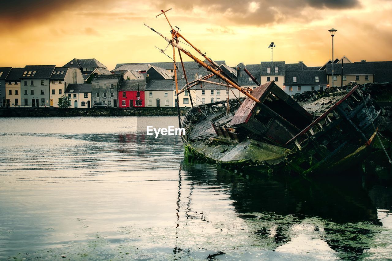 Old wooden sunken ship at sunrise in corrib river galway city ireland, colorful houses in background 