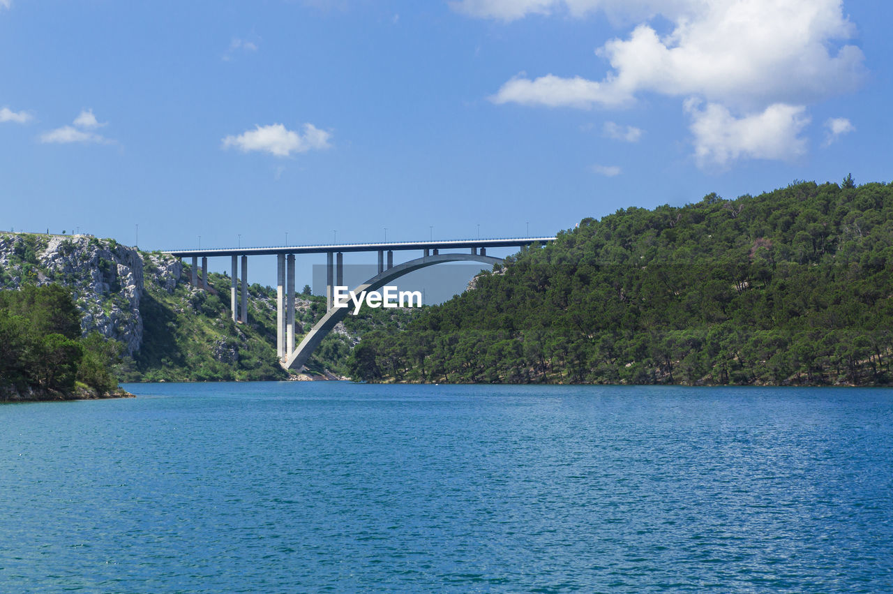 Bridge over a bay with wooded hills under a summer sky.