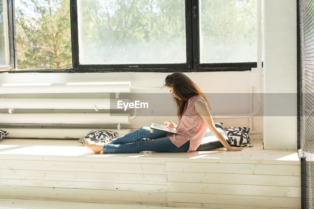 Side view of woman sitting on window