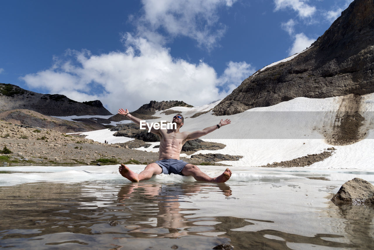 Man sitting in lake against mountains during winter