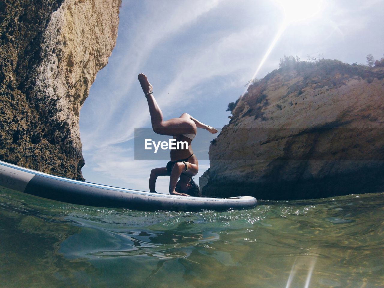 Young woman doing headstand on paddleboard against sky