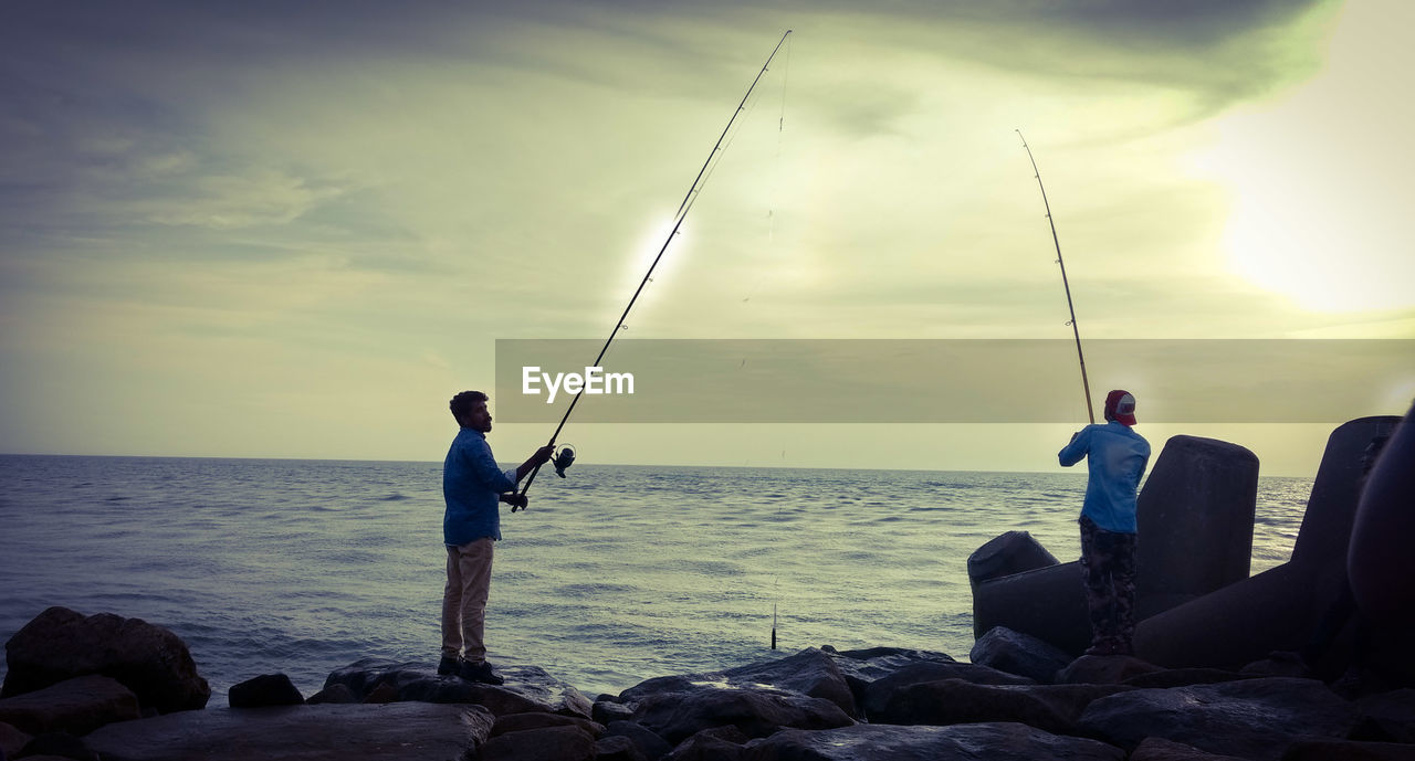 MAN FISHING ON ROCK AGAINST SEA