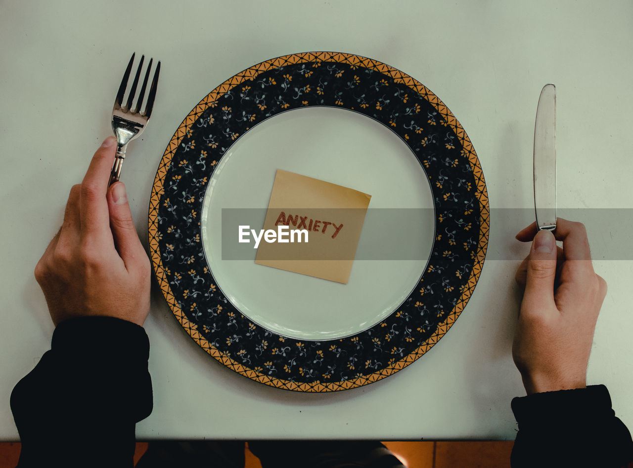 Cropped hands of person cutlery by plate with text on adhesive note over table