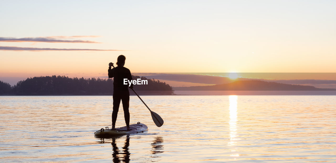 SILHOUETTE MAN STANDING IN WATER AT SUNSET