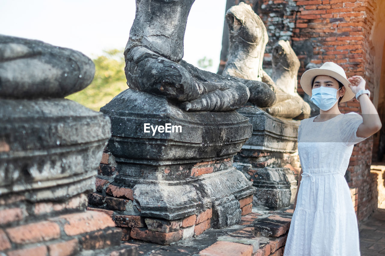 Mid adult woman wearing mask looking away while standing against ancient structure