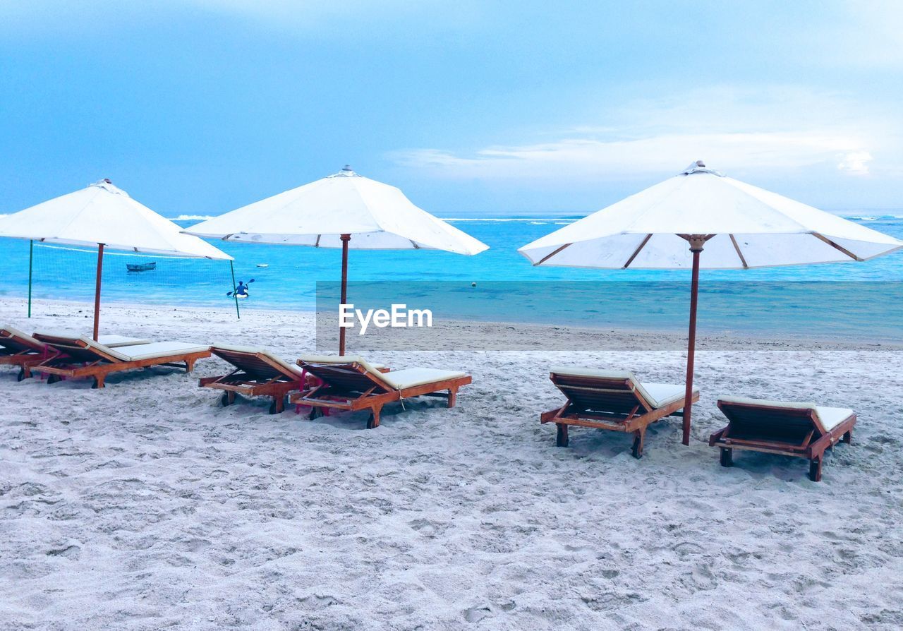 Deck chairs on beach against sky