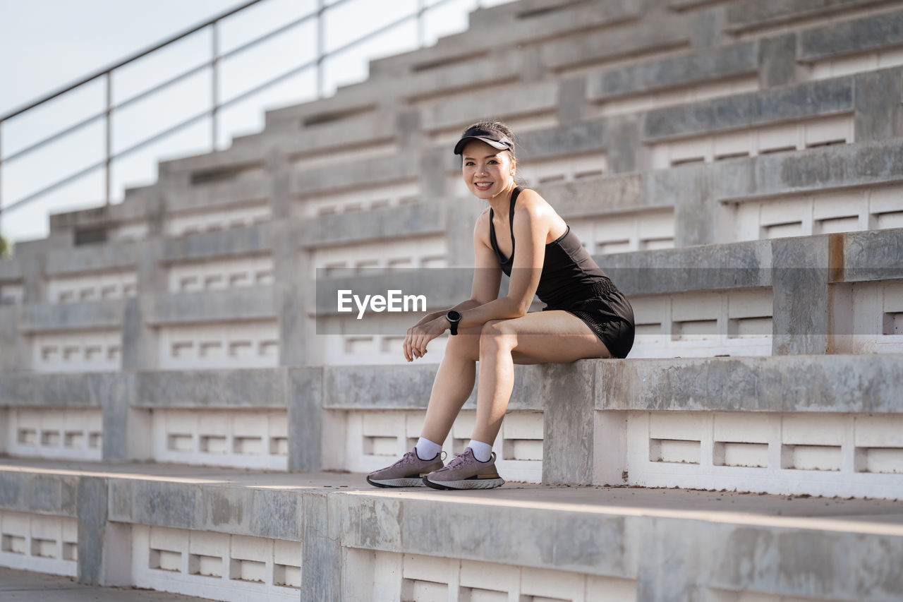 FULL LENGTH OF WOMAN SITTING ON RAILING