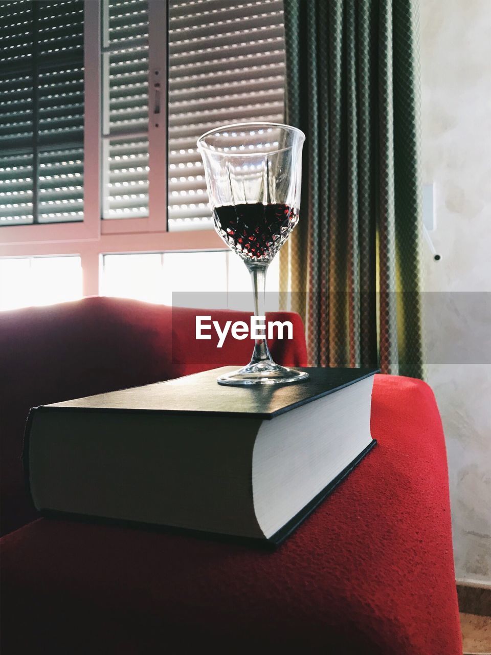 CLOSE-UP OF WINE GLASS ON TABLE AGAINST WINDOW