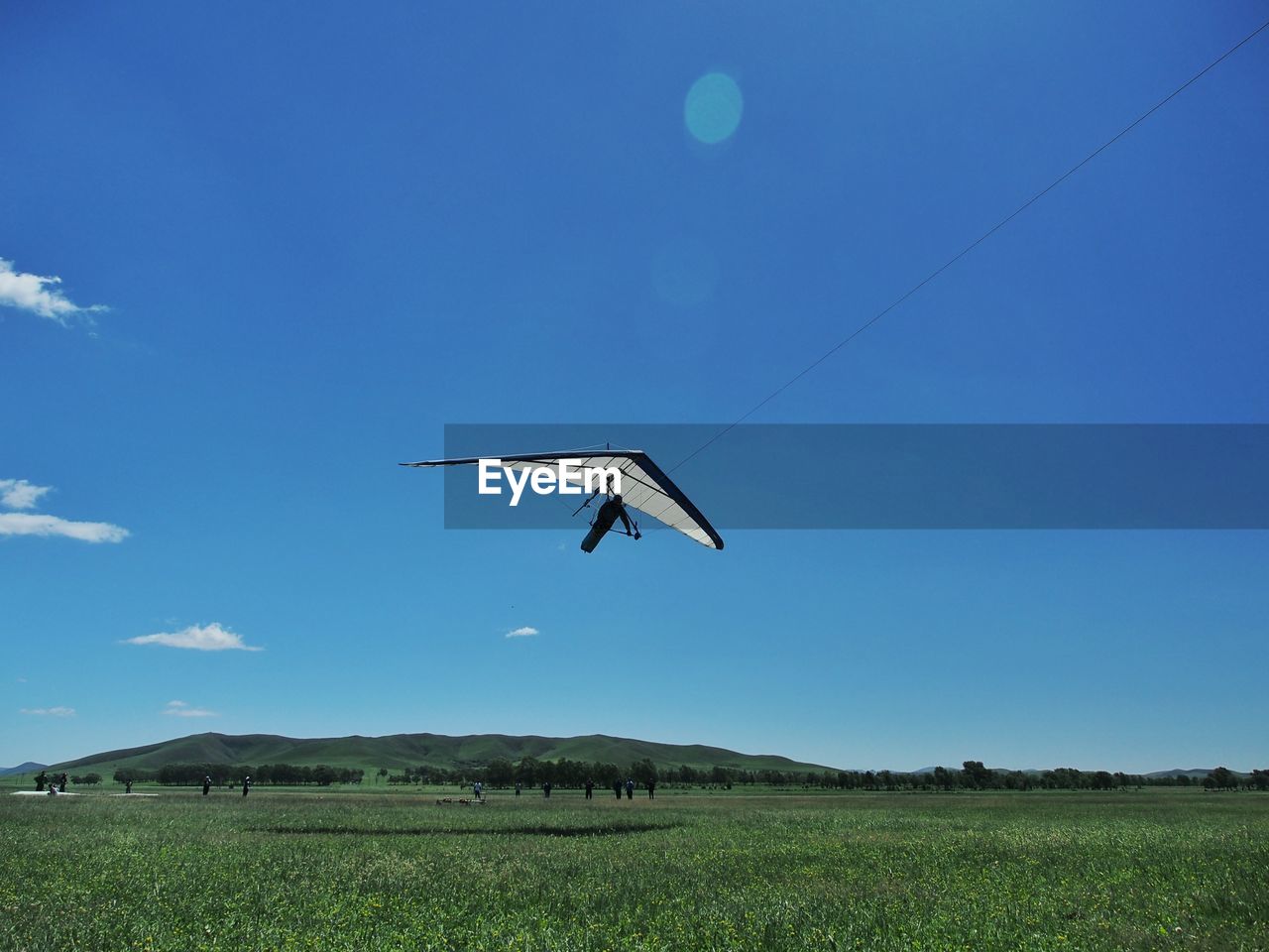 Person hang-gliding over field against clear blue sky