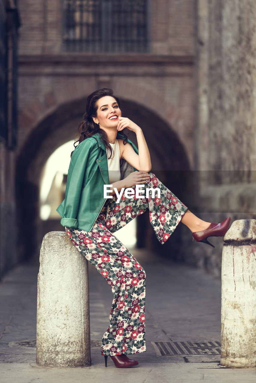 Portrait of smiling young woman sitting on bollard