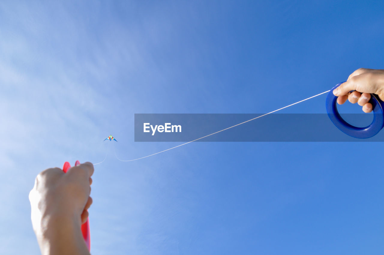 Low angle view of hand holding kite against blue sky