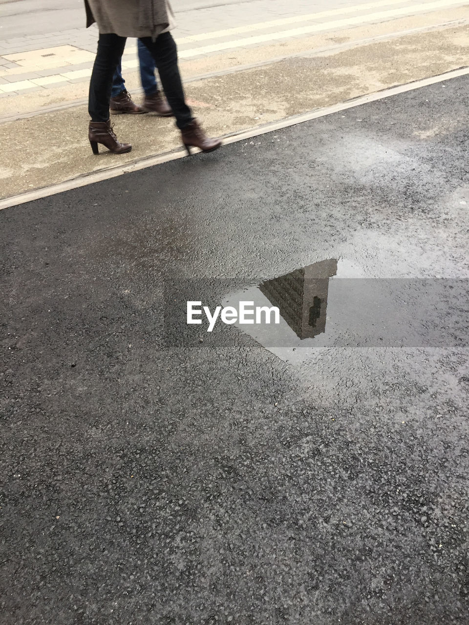 Low section of man and woman walking on road by puddle with reflection