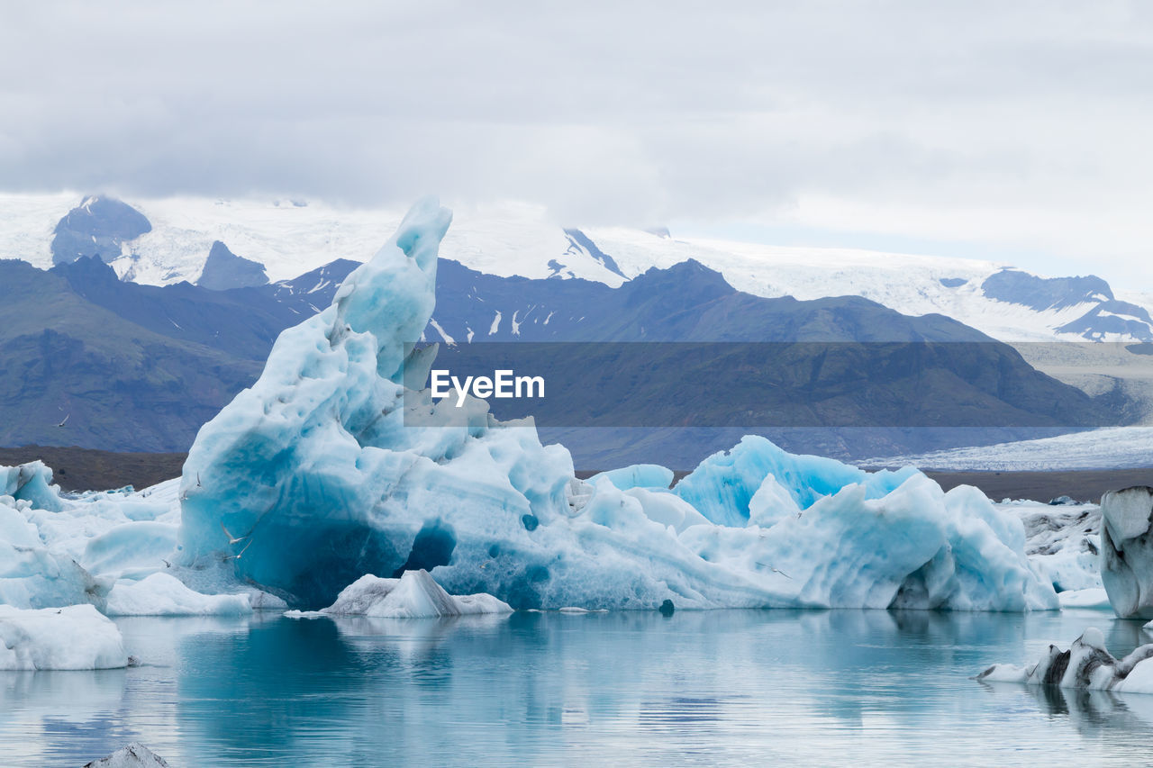 ICE FLOATING ON WATER AGAINST MOUNTAIN