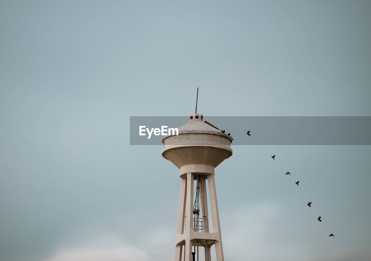 Low angle view of birds flying by tower against sky