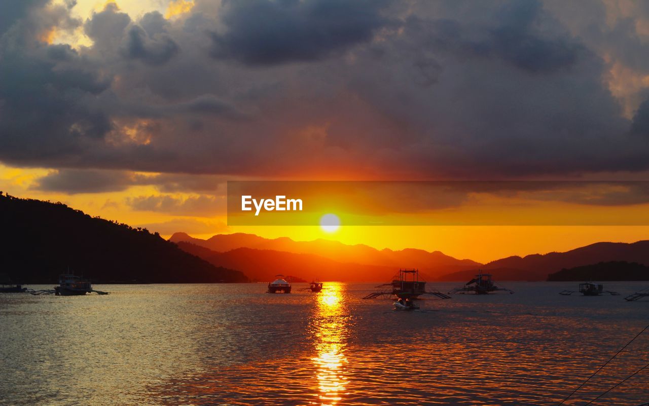 SILHOUETTE BOATS IN SEA AGAINST ORANGE SKY