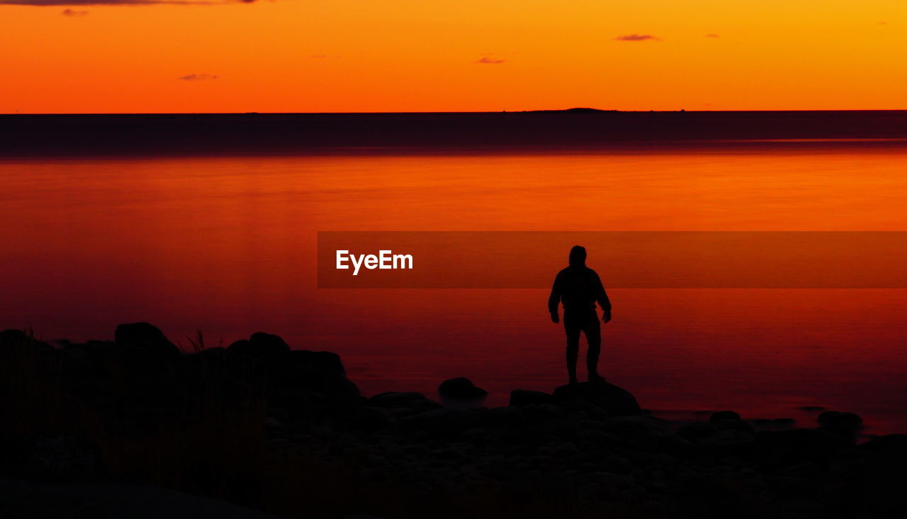 Silhouette man standing on rock against orange sky