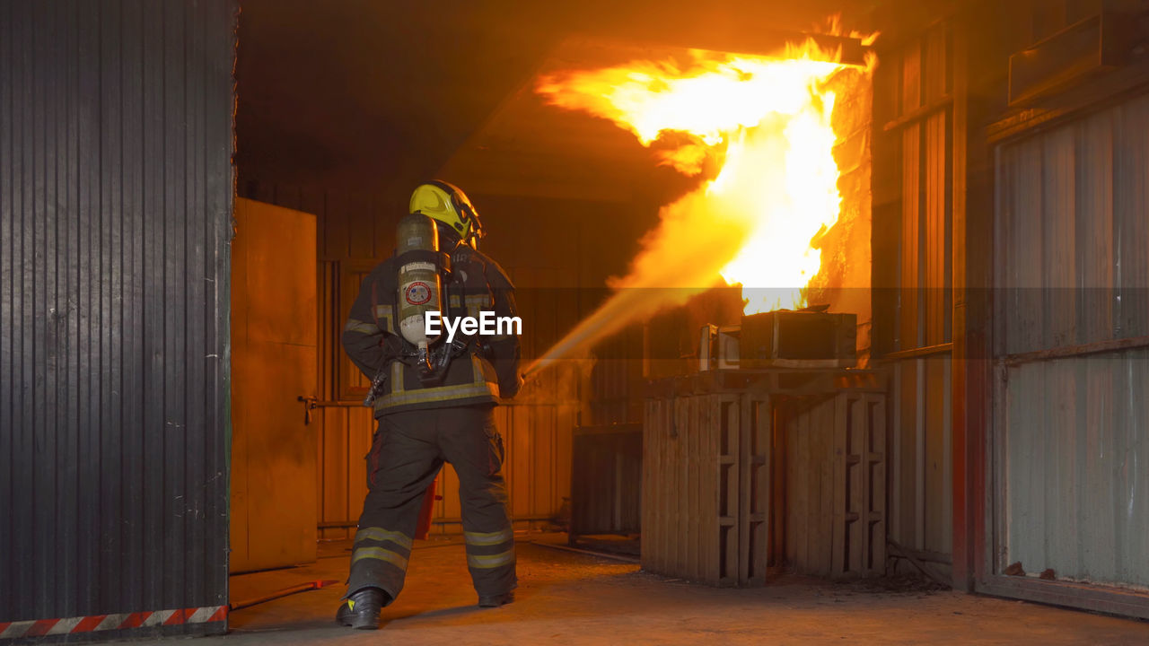 MAN STANDING BY FIRE ON BUILDING AT NIGHT