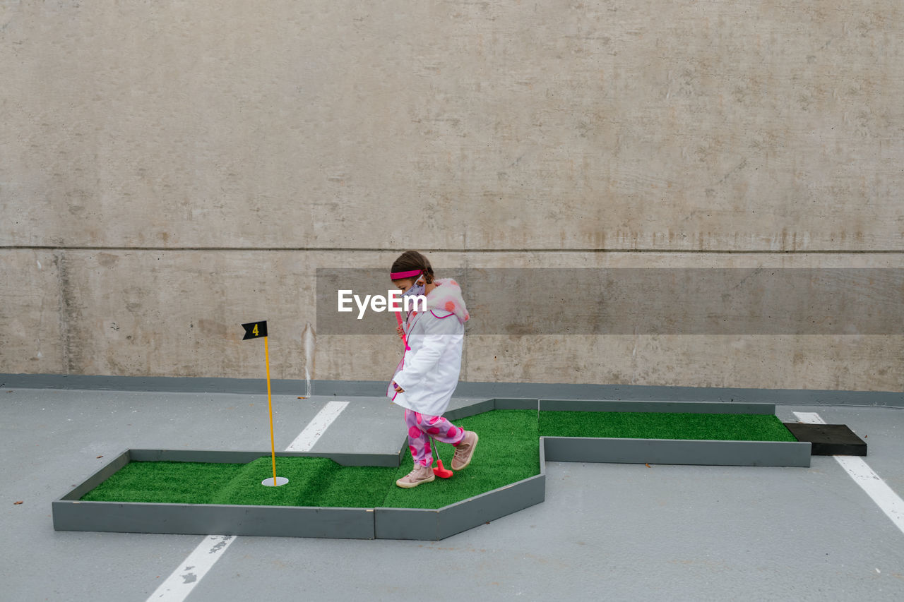 Girl in pink doctor costume and face mask playing mini golf