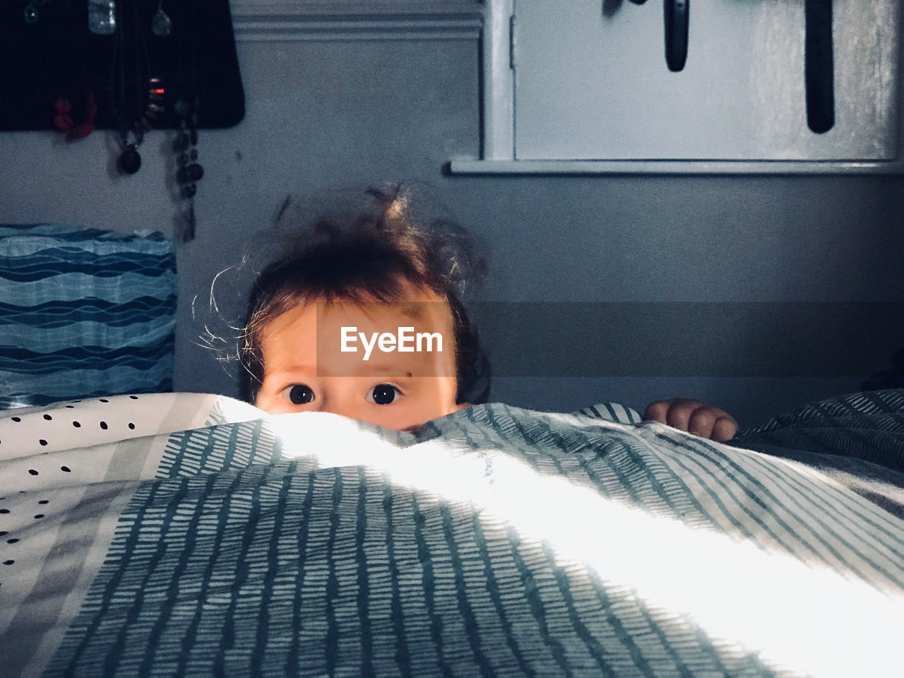 Portrait of cute baby girl hiding behind bed at home