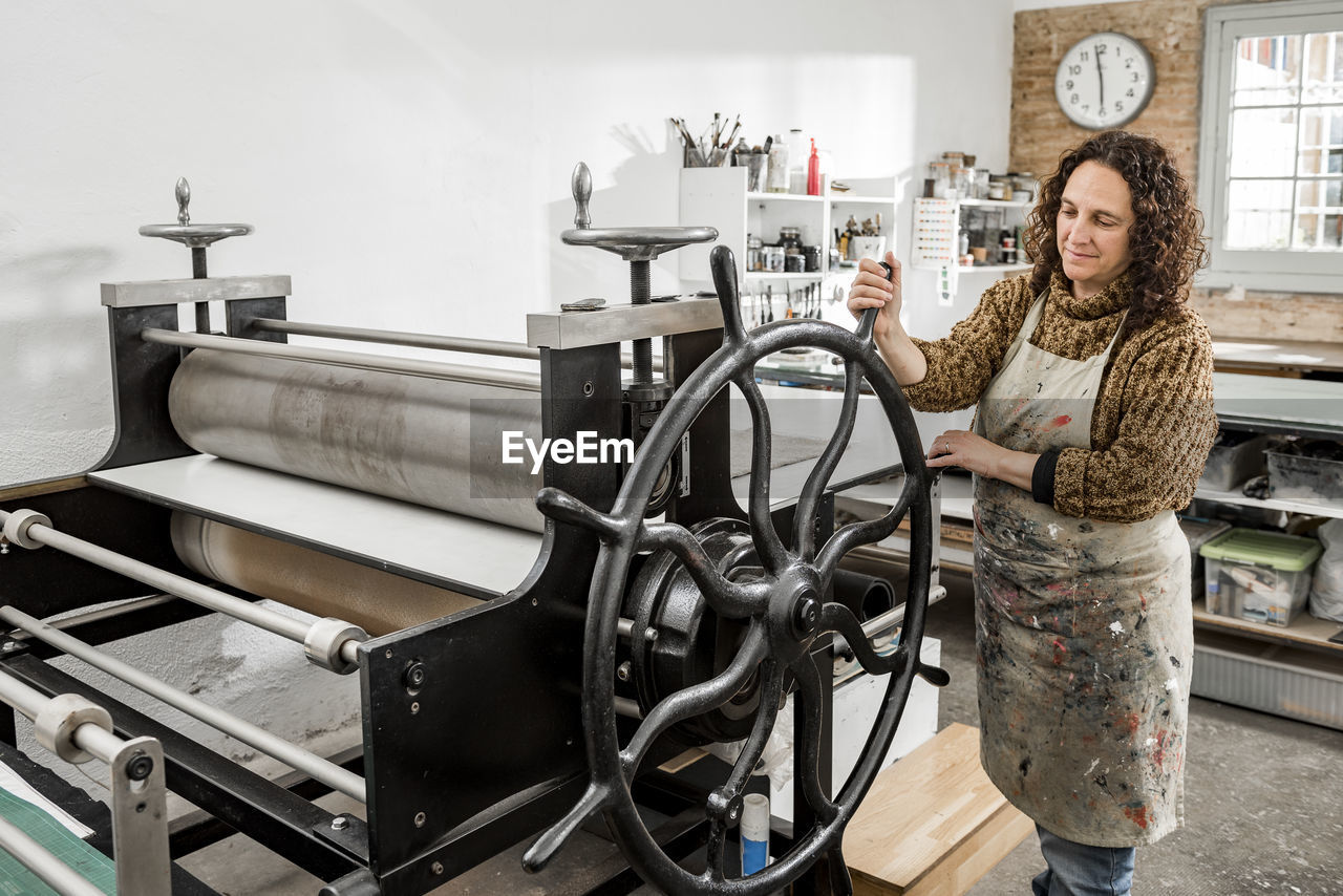 Female artist operating a manual vintage industrial printer.