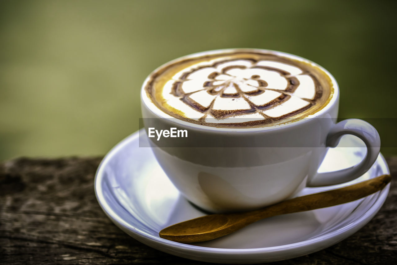 A white cup of hot coffee with latte art, serving on wooden table