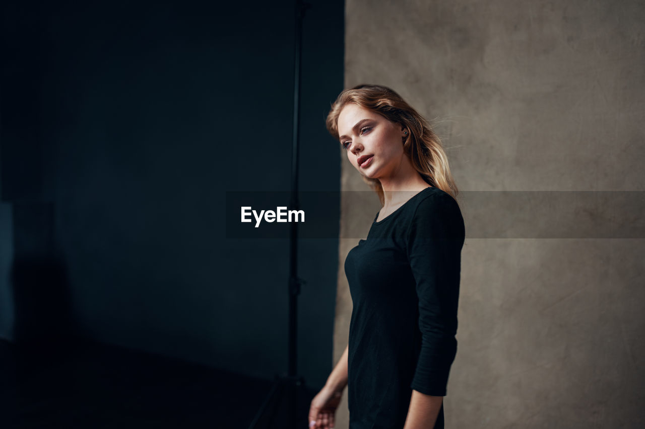 Young woman looking away while standing against wall