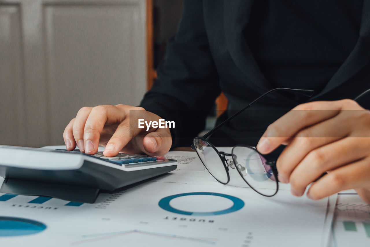 Midsection of businesswoman using calculator at office