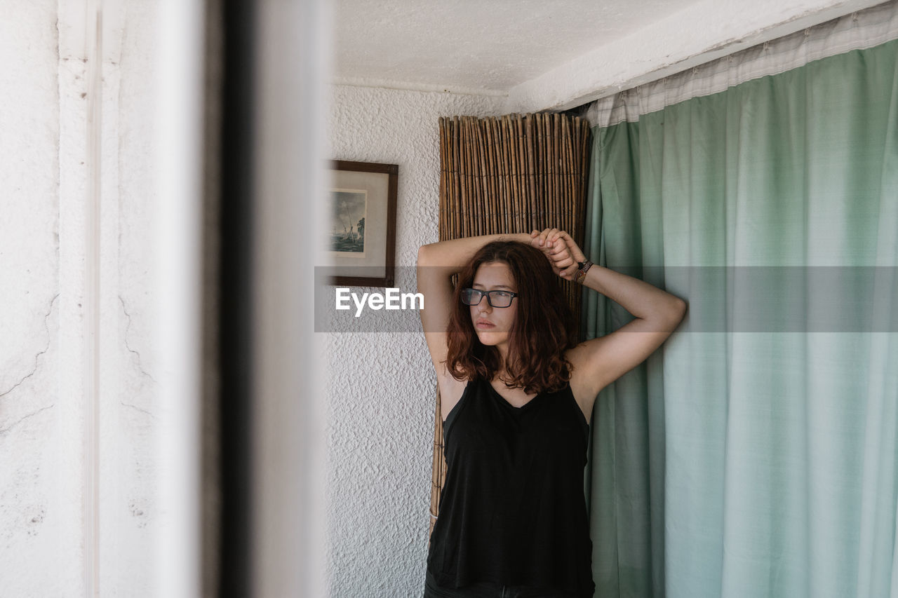 PORTRAIT OF YOUNG WOMAN STANDING AGAINST CURTAIN