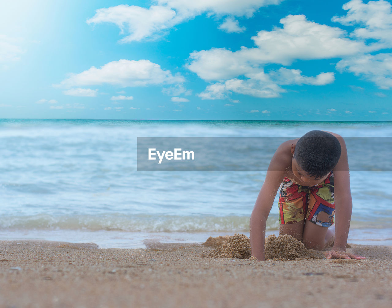 Boy digging sand at beach against sky