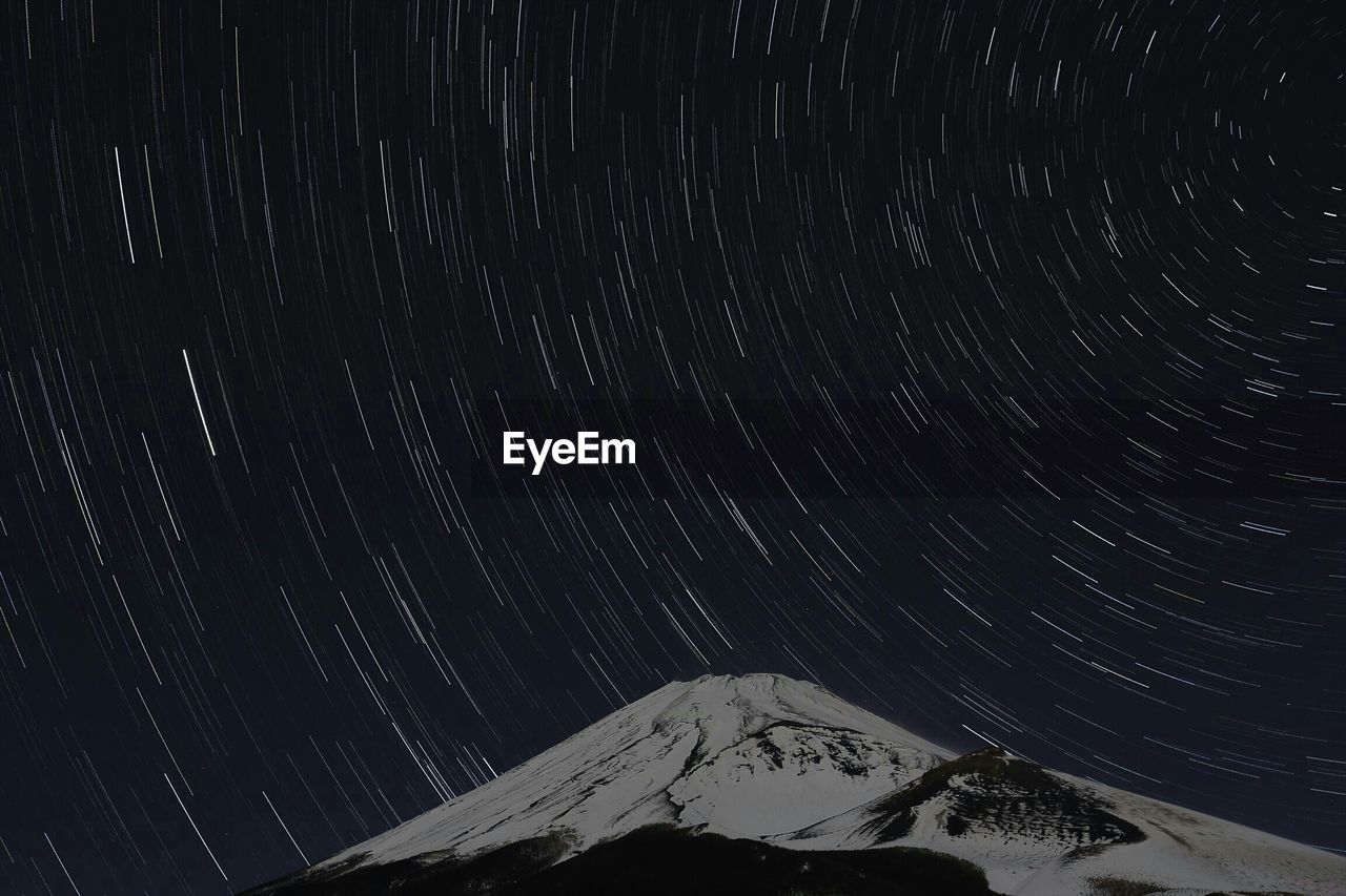 Idyllic view of star trails over snowcapped mountain