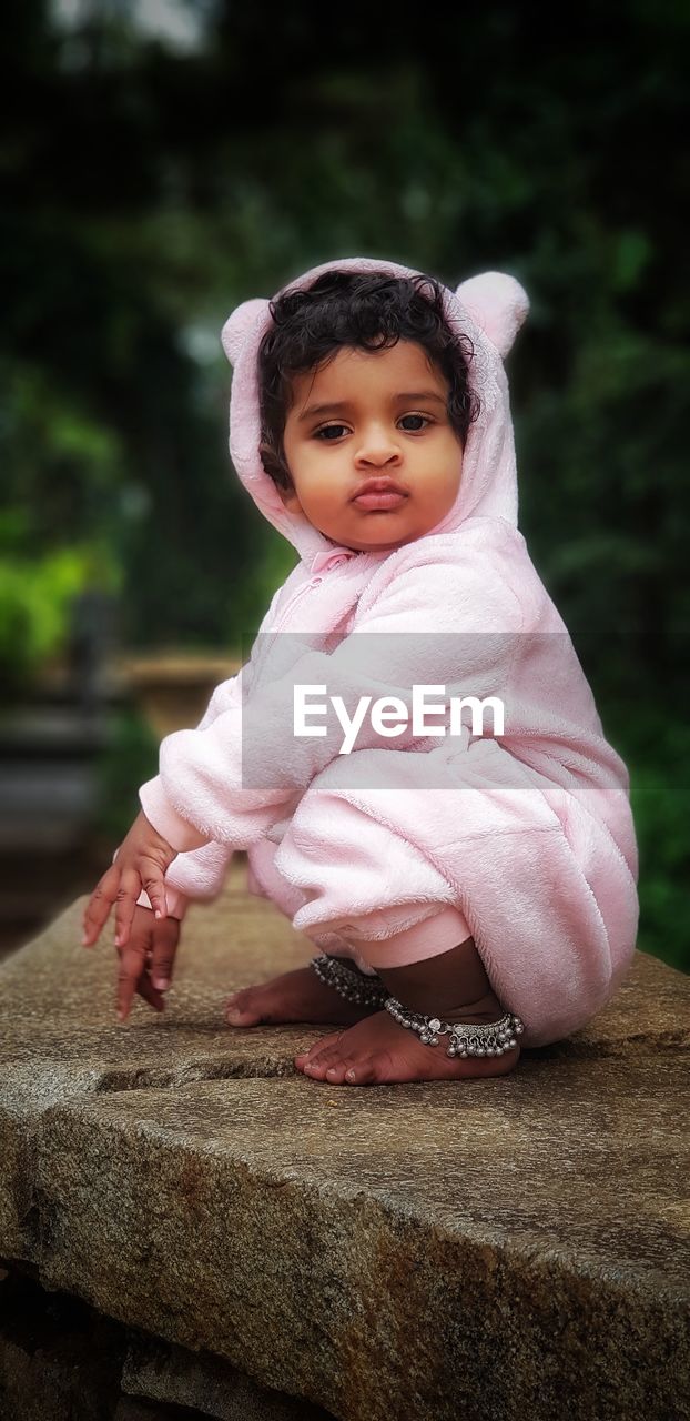 Portrait of cute baby girl crouching on retaining wall