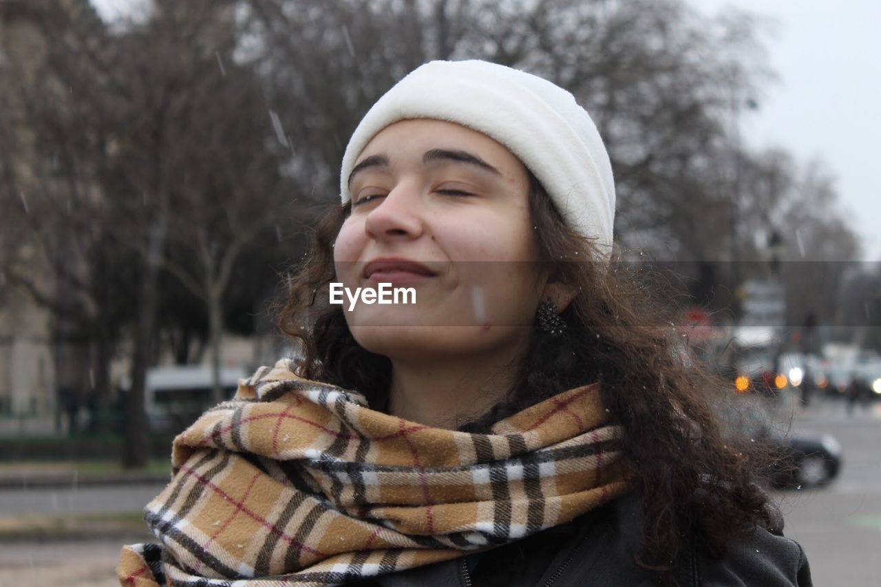 Smiling young woman with eyes closed standing outdoors during winter