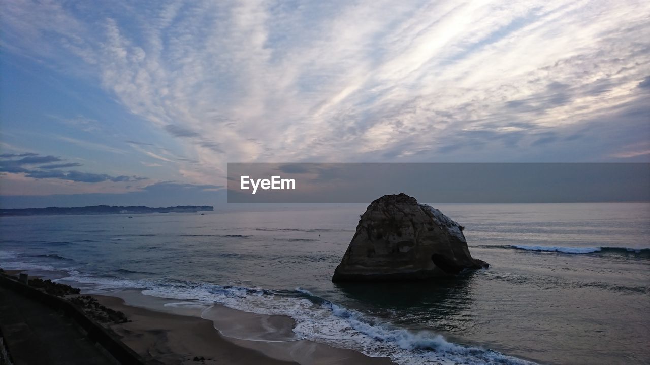 ROCK FORMATION ON SEA SHORE AGAINST SKY