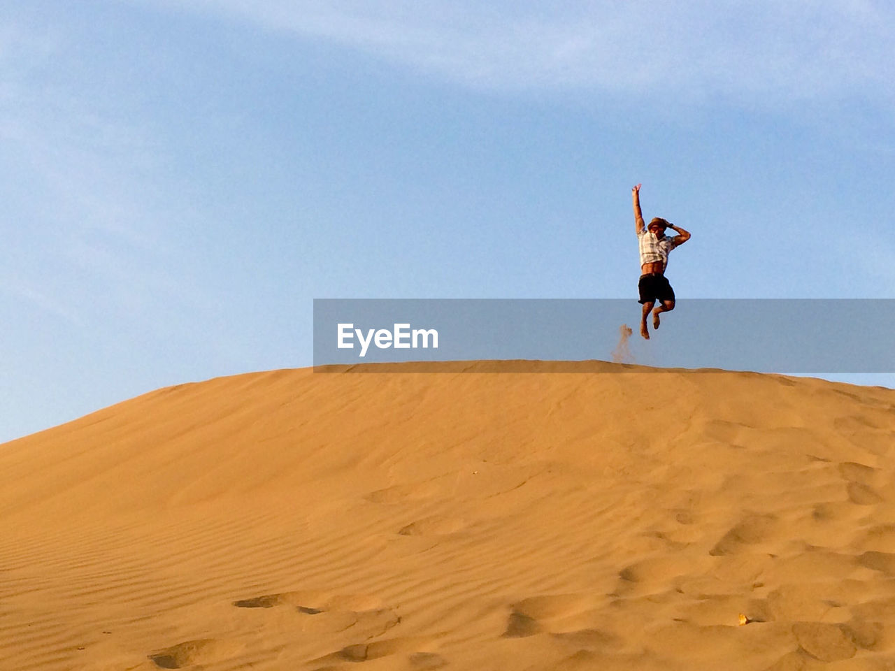 Full length of man jumping over sand dunes against sky