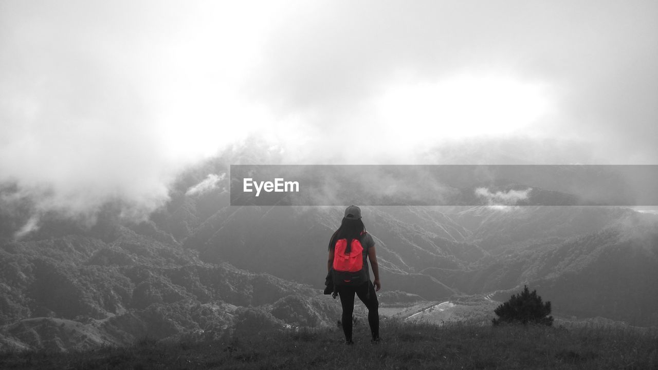 REAR VIEW OF PERSON STANDING ON MOUNTAIN AGAINST SKY