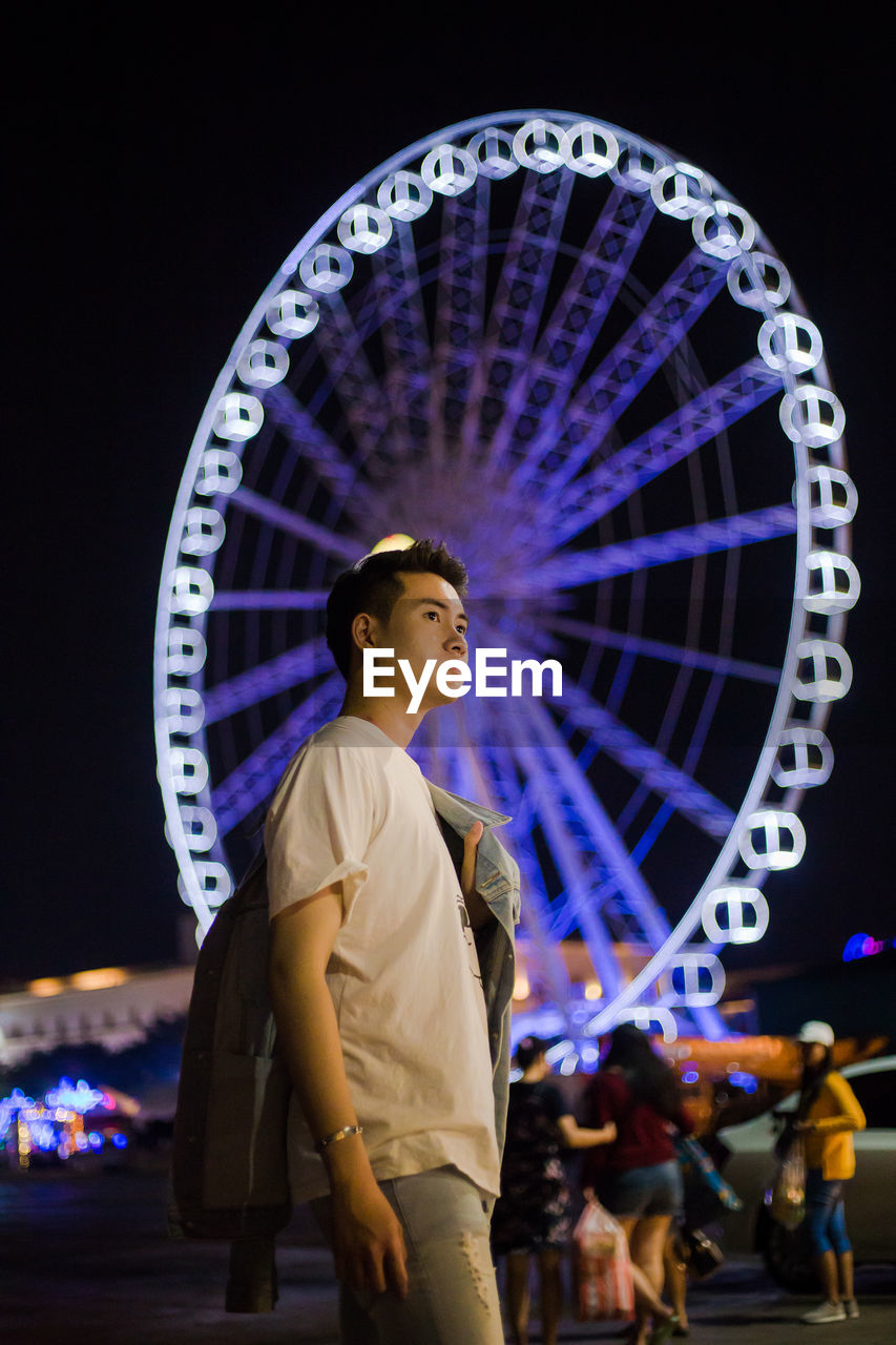 Man standing in illuminated amusement park at night