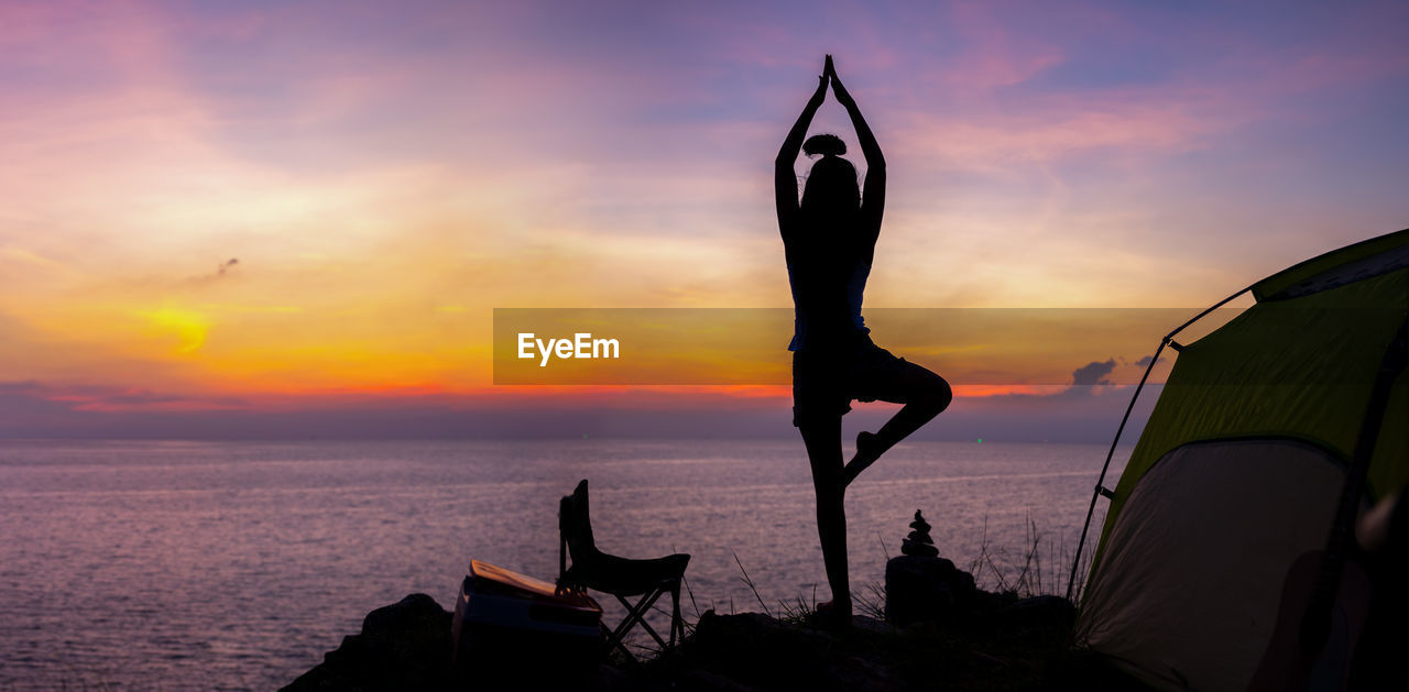 Silhouette young woman meditating by sea against sky during sunset