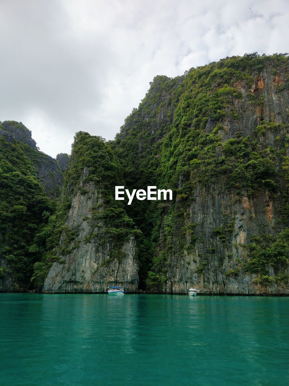 Scenic view of sea by mountain against cloudy sky