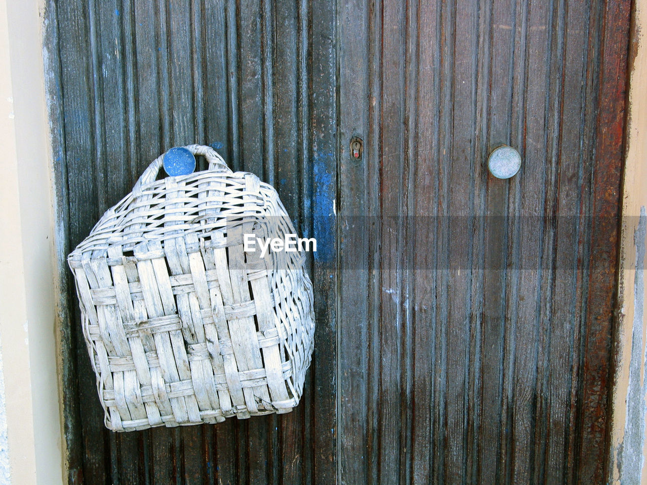 Old basket hanging on the old door handle. 
closeup of the basket and door. cinqueterre, italy.