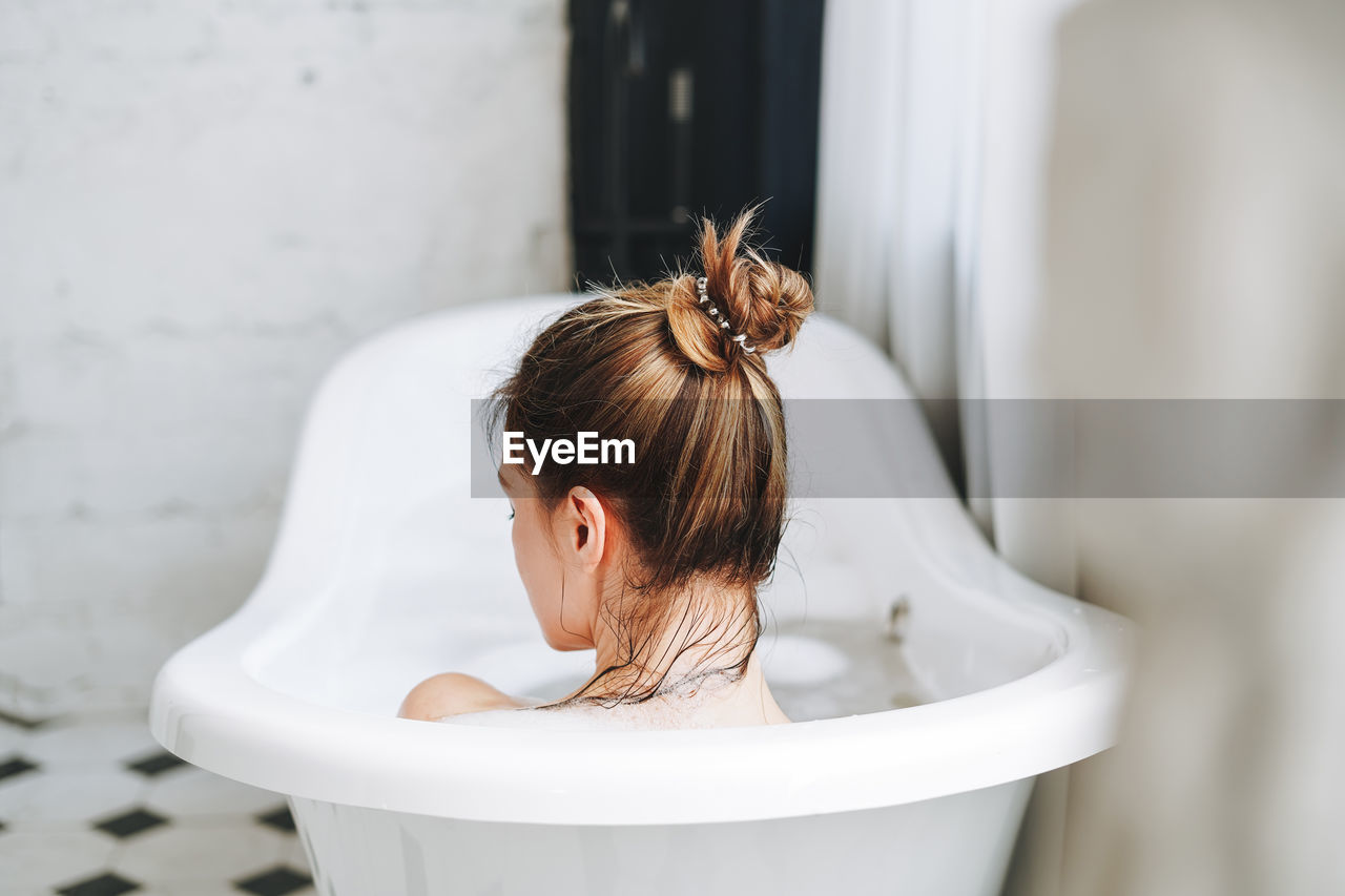 Young happy woman taking bath with foam at home, treat yourself