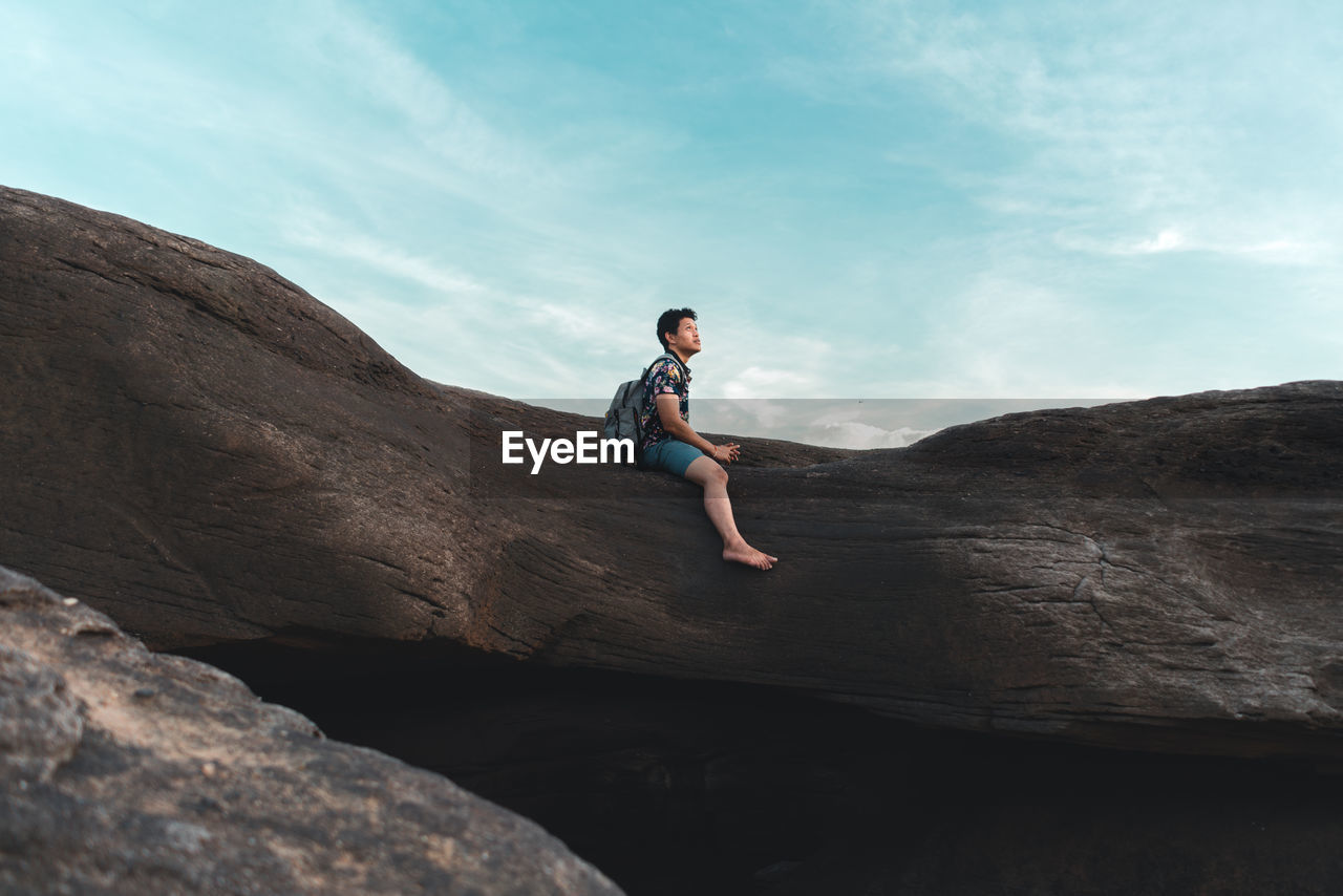 Side view of man on rock against sky