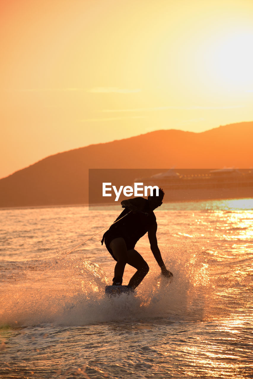 Side view of man wakeboarding against sky during sunset